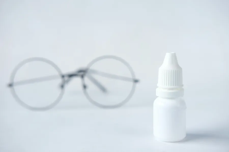 Eyeglasses beside a bottle of eye drops